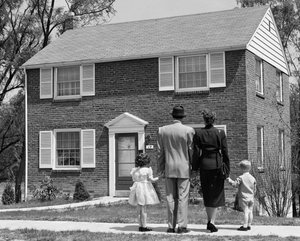 A family stands in front of a 1950s home without a front porch.