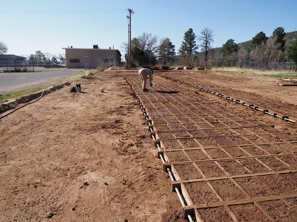 Adobe bricks lay in the sun to dry. A student working on the house pours water into the cracks to seal them.