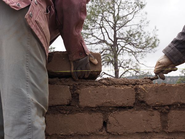 Students work together to trowel mud across a brick before placing another one, which will be leveled to the height of the yellow string.