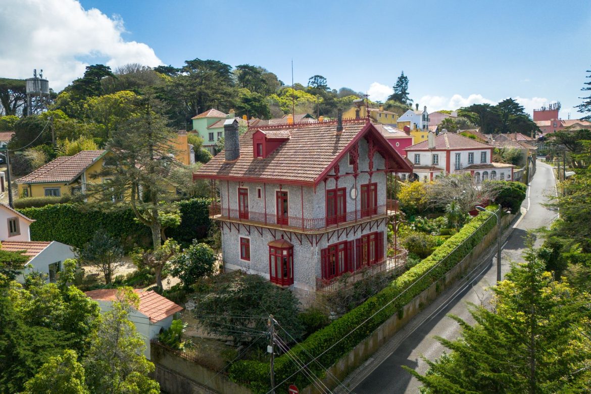 surrounded-by-gardens-on-a-hilltop-overlooking-the-ocean-this-historic-home-has-a-stone-facade-bright-red-accents-and-whimsical-interiors-with-ornate-molding-and-parquet-floors.jpg